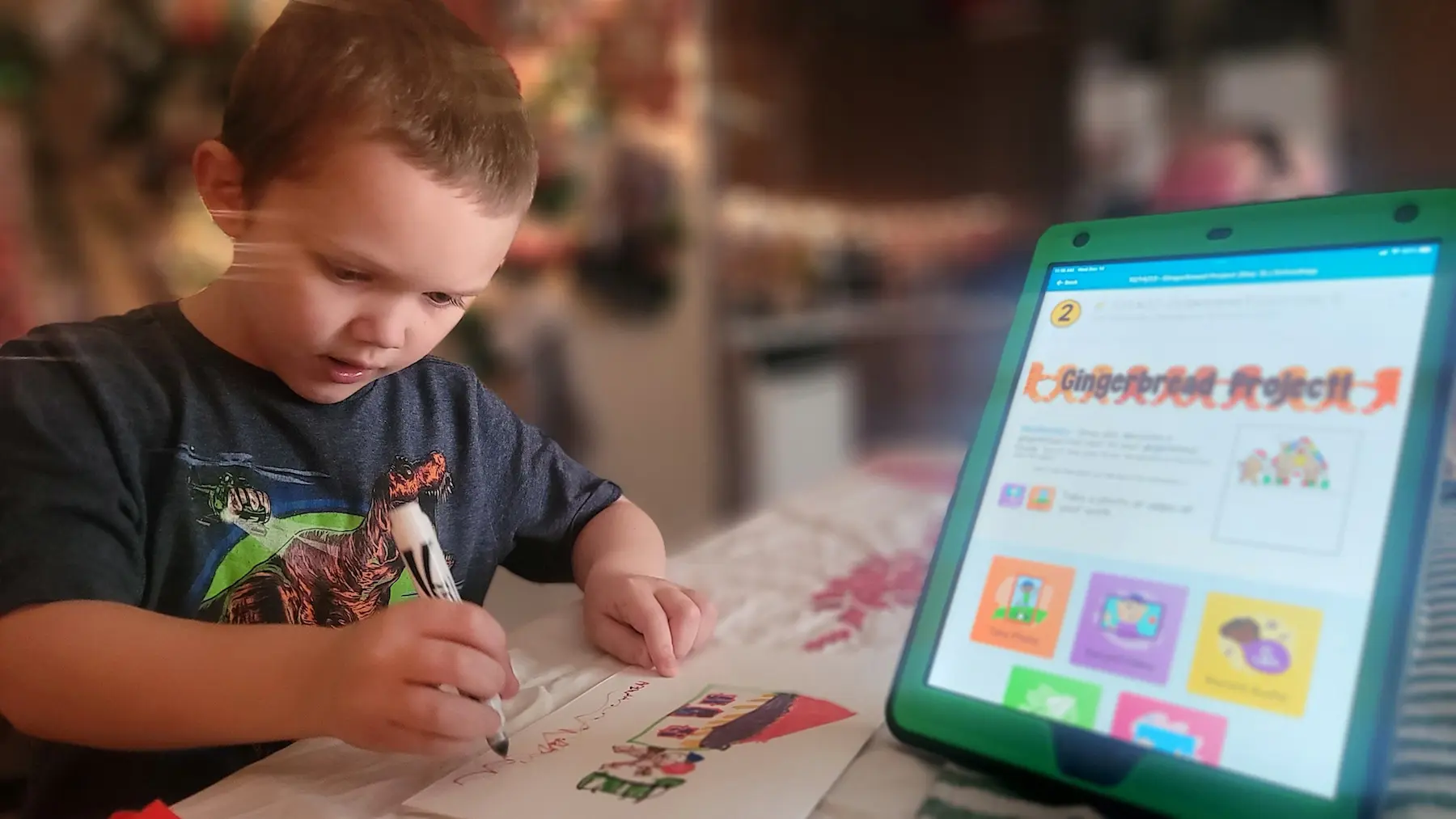 An Insight PA student is coloring a picture of a house at their home work station. There is a tablet on the desk that shows instructions for the school project they are working on.