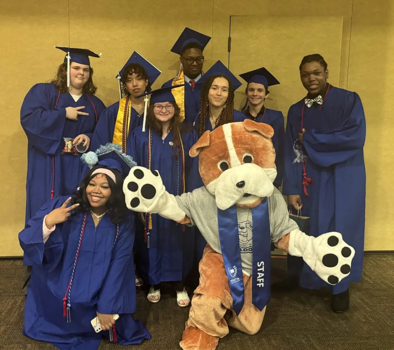 A group of Insight PA graduates is posing in their caps and gowns with the school’s bulldog mascot.