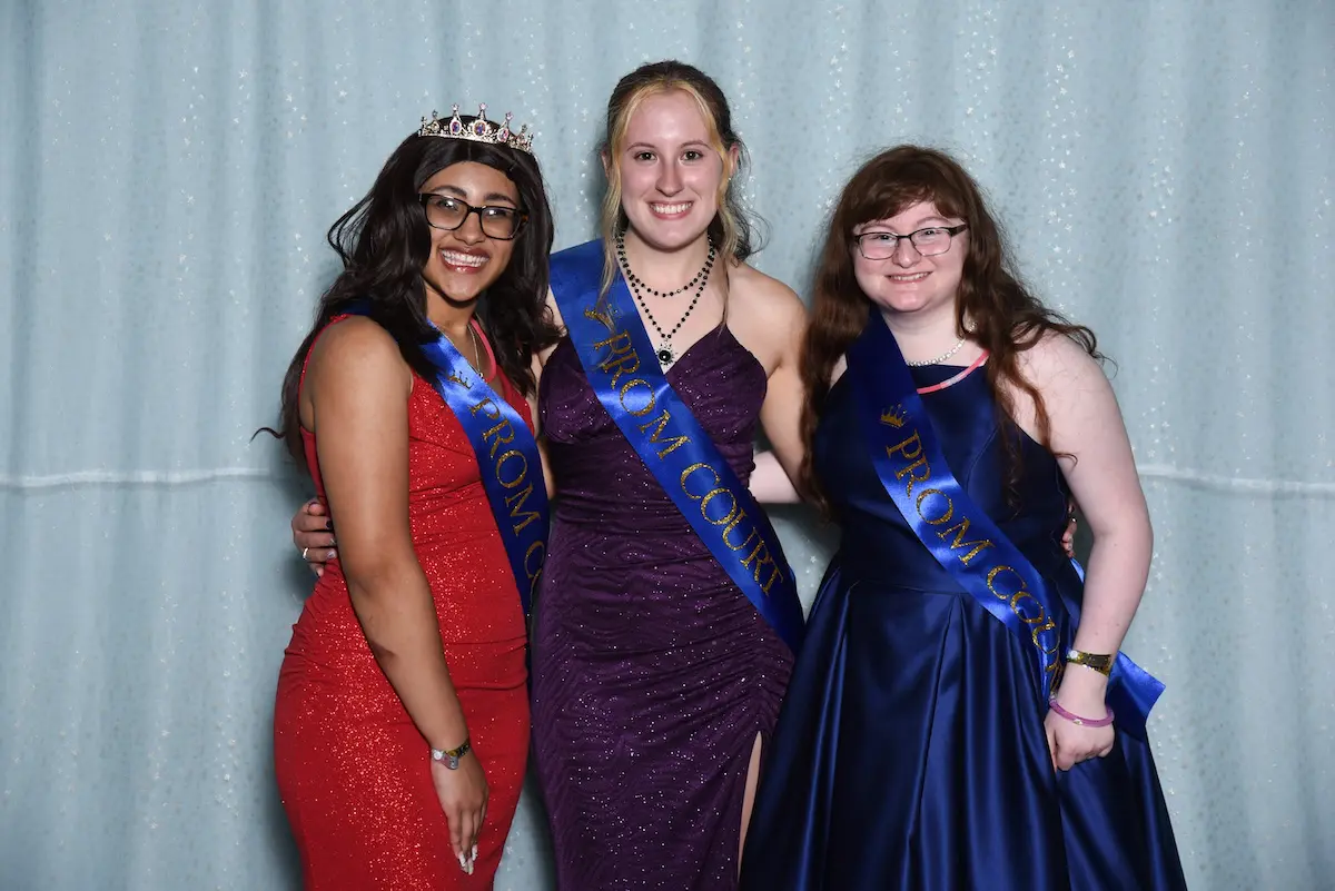 Three students pose in prom dresses and sashes
