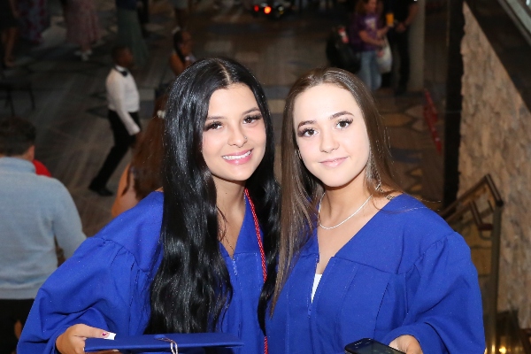 Two Insight PA Cyber Charter School grads are wearing graduation gowns and holding their caps in front of themselves.