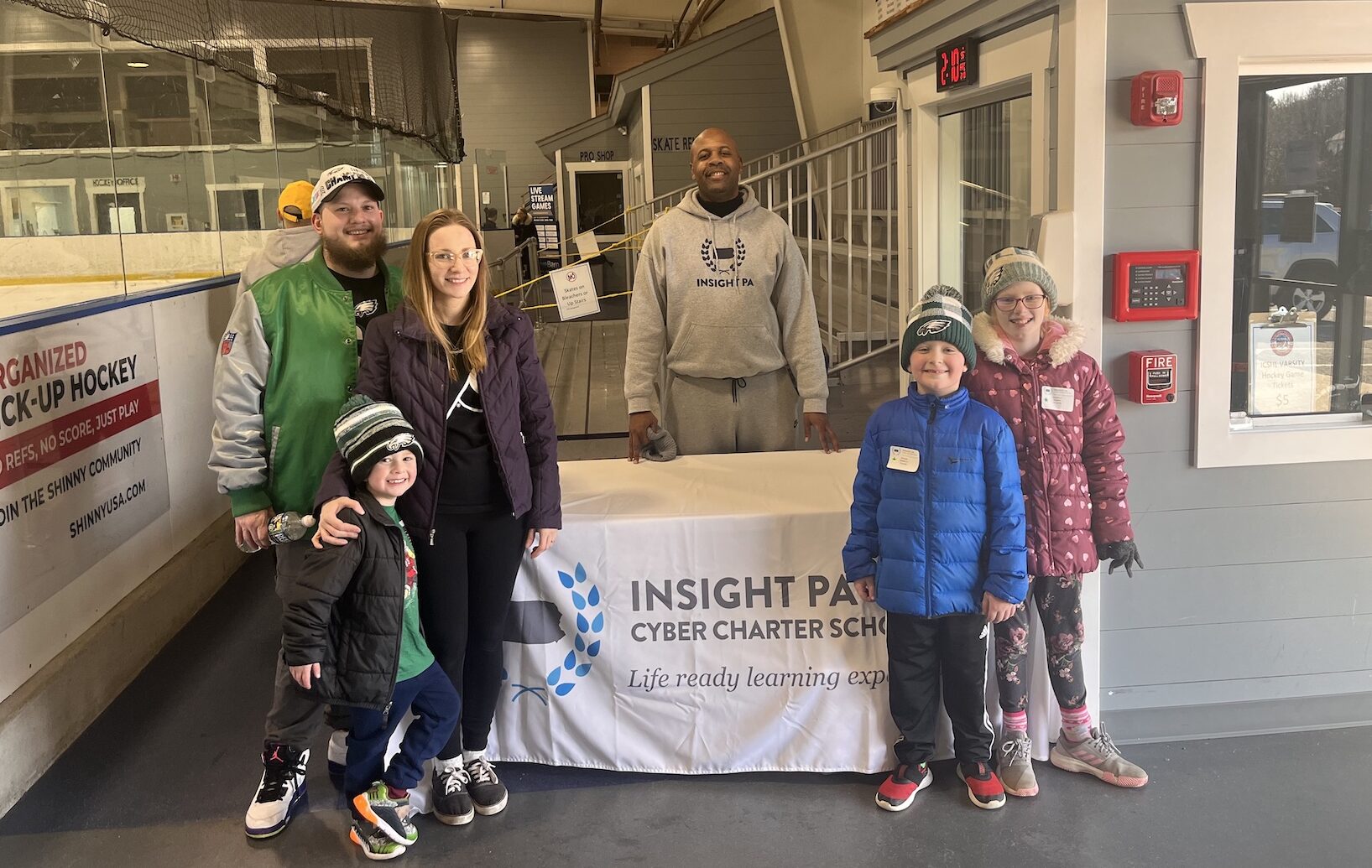 Insight PA students and family members are at a skating event. They are standing at a table that says Insight PA with a staff member behind the table.