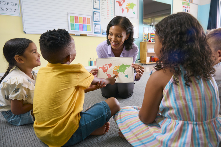 Stock image of a student working with a classroom of elementary students.