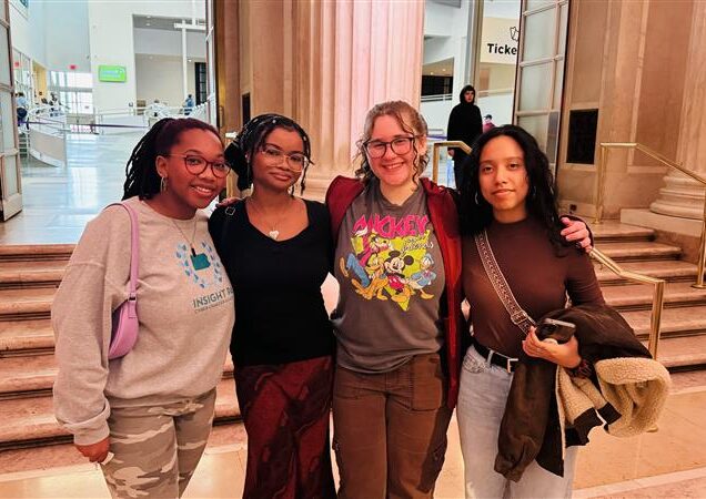 A group of students pose in front of a staircase with their arms around each other.